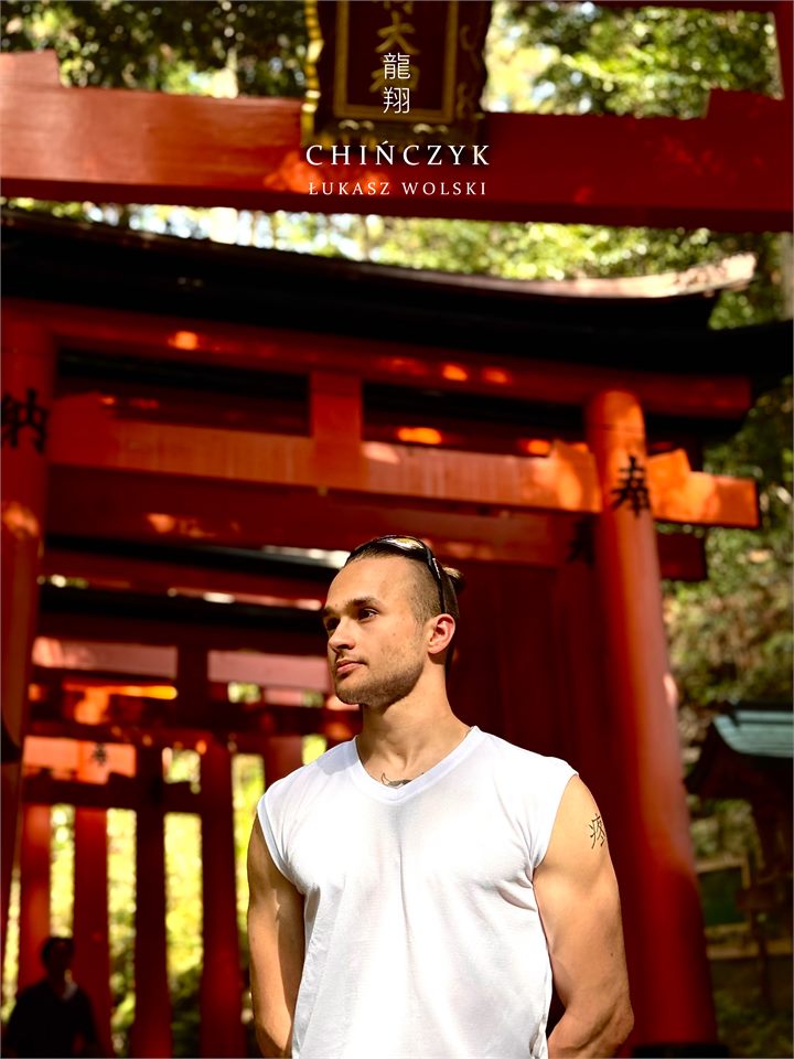Łukasz Wolski na tle czerwonych bram torii w Japonii